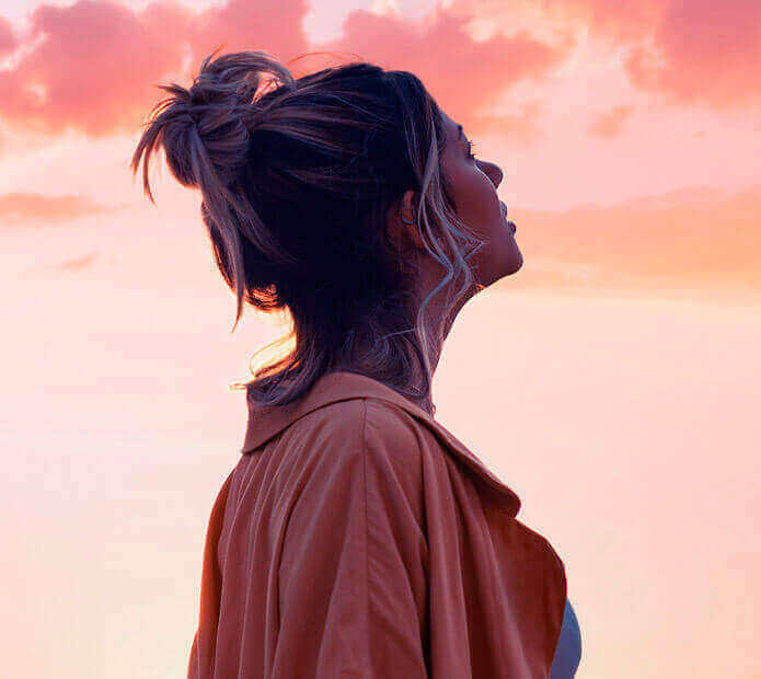 Uma mulher olhando para o céu com a luz de um final de tarde